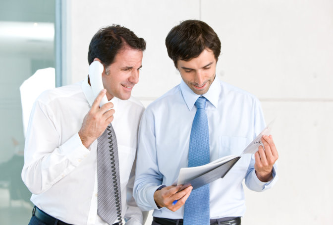 Two colleagues reviewing paperwork while taking a phone call